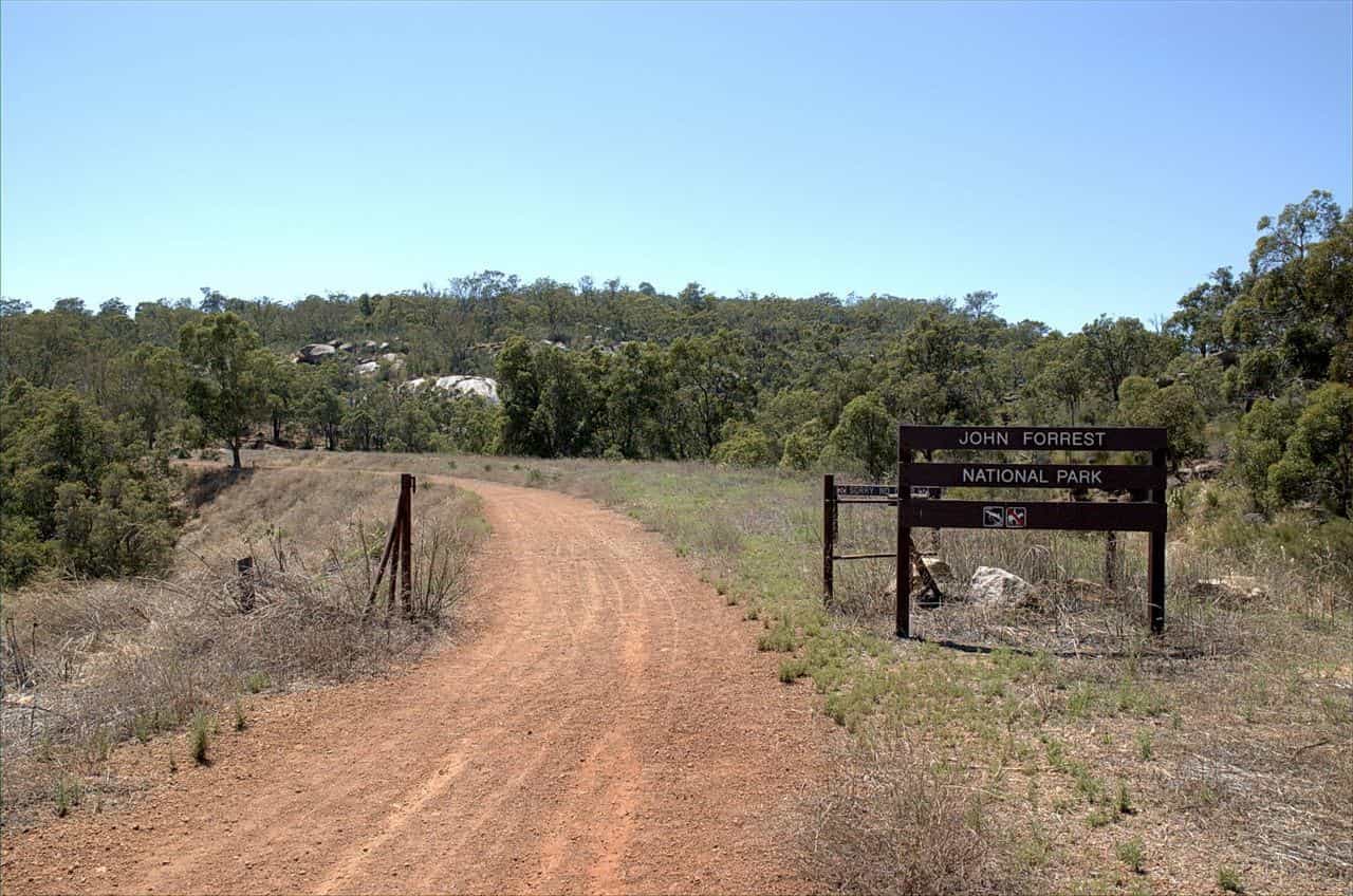 A dirt track leading past a park sign into eucalypt bushland in John Forrest National Park