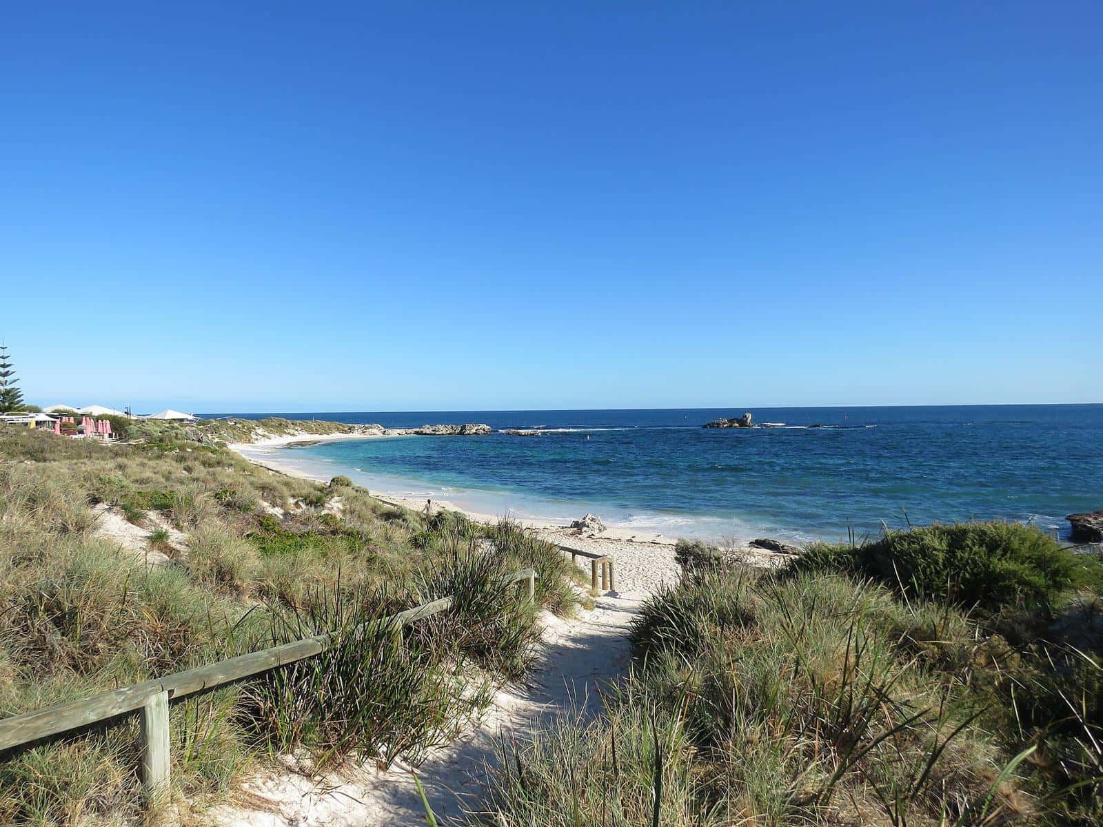 A sandy path between shrubs leading to a clear blue bay on Rottnest Island